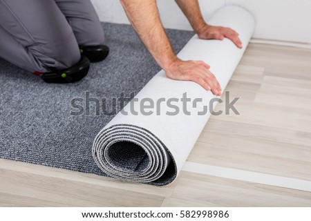 Close-up Of Worker's Hands Unrolling Carpet On Floor At Home