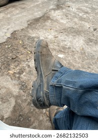 Close-up of a worn work boot resting on the ground, paired with blue jeans. A rustic and authentic capture that conveys simplicity, resilience, and the passage of daily labor.