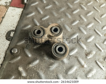 Close-up of a worn-out motorcycle linkage bearing part placed on a textured metal surface. Used mechanical component from a motorbike suspension system.