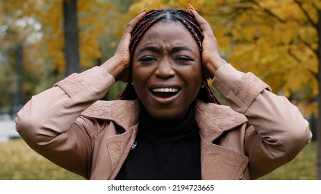 Close-up worried anxious young woman standing outdoors shouting loudly in rage covers ears with palms from noise annoyed frustrated girl feels stress hopelessness holding head suffering from - Shutterstock ID 2194723665