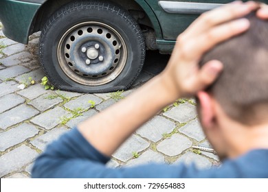 Close-up Of A Worried Man With Hand On Head Looking At Punctured Car Tire