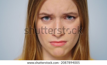 Closeup worried woman face looking camera on grey background. Portrait upset model face indoors. Close up unhappy girl posing in studio. Stressed lady concept. Exhausted sad girl face expression