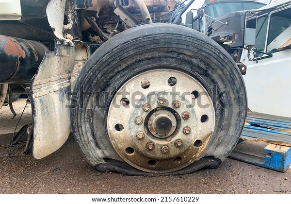 Closeup of wrecked\
truck wheel with a punctured or flat tire at a car junkyard after a\
traffic accident