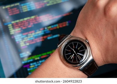 Close-up of a wristwatch showing binary digits instead of hour numbers on a programmer’s wrist, with blurred laptop screen and code in the background — symbol of deep coding immersion.