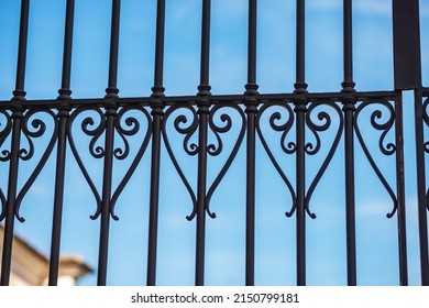 Close-up of a wrought iron gate against a blurred clear blue sky with clouds. Brescia, Lombardy, Italy, Europe.