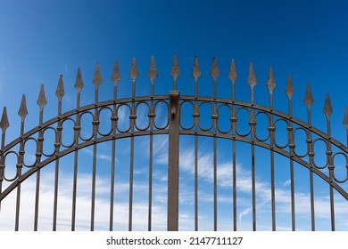 Close-up of a wrought iron gate with sharp points on blue sky with clouds and copy space.
