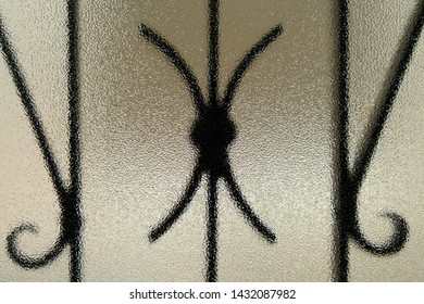 Close-up Of Wrought Iron Window Bars Through Frosted Textured Glass Seen From The Inside Looking Out.