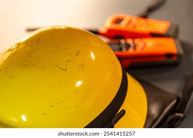 A close-up of a yellow firefighter helmet rests on a table, with two radios blurred in the background, ready for emergency communication during a fire alarm.  - Powered by Shutterstock