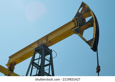 Close-up Of A Yellow Oil Rig Pumping Oil Against A Blue Sky. View From Below. Extraction Of Black Gold From The Well