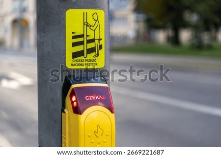 Close-up of a yellow pedestrian push button with a red WAIT light and a yellow sticker explaining to press it to cross, crucial for street safety