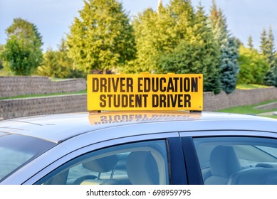 Closeup of yellow student driver sign on top of silver drivers ed car in high school parking lot