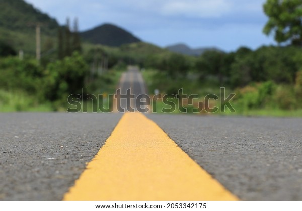 Close-up of the yellow traffic line in the\
middle of the road and blurring the foreground to reveal the road\
and faint mountains.