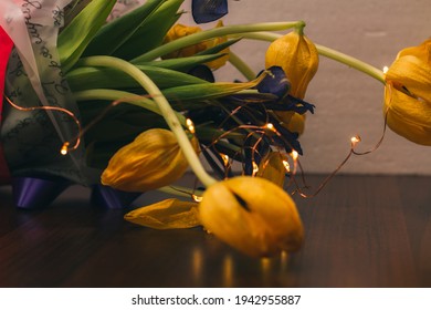 Close-up Of Yellow Tulips On The Table In The House. Garden Flowers. A Bouquet Of Tulips And Christmas Lights. Gift