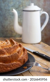 Close-up Of Yogurt Sponge Cake On Dark Plate, With Wooden Fork, Knife And Old White Coffee Pot, On Wooden Table, Selective Focus, Vertical