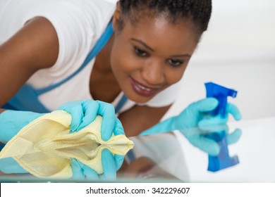 Close-up Of Young African Woman Using Spray To Wipe Glass Desk