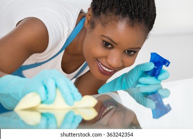 Close-up Of Young African Woman Using Spray To Wipe Glass Desk