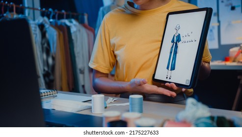 Close-up young Asia lady dressmaker use digital tablet meeting with designer discuss show sample dress design new collection on screen on desk in shop at night. Tailor new business startup concept. - Powered by Shutterstock