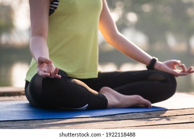 Closeup Of A Young Asian Beautiful Woman Practicing Yoga And Meditate In The Lotus Pose Outdoor Beside The Lake In The Morning For Relaxation And Peace Of Mind. Harmony And Meditation Concept.