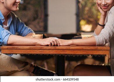 Closeup of young Asian couple holding hands affectionately on date in cafe