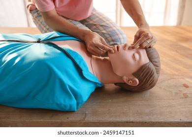 Close-up of young Asian female hands performing cardiopulmonary resuscitation (CPR) on a training dummy. Key elements include defibrillator, compressions, mouth-to-mouth, and abdominal thrusts. - Powered by Shutterstock