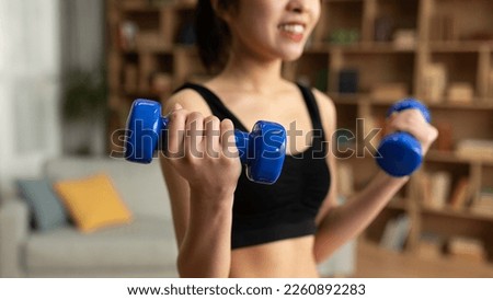 Closeup of young asian lady doing dumbbell workout at home, working on arms strength, cropped. Korean woman lifting blue fitness dumbells up, living room interior