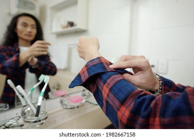 Close-up Of Young Asian Man Adjusting Checkered Shirt Sleeve While Getting Dressed In Front Of Mirror In Bathroom