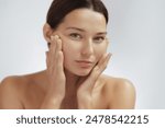 Close-up of a young Asian woman inspecting her skin, touching her face with a thoughtful expression. Ideal for beauty, skincare, wellness, plastic surgery, and face lift themes. High quality image