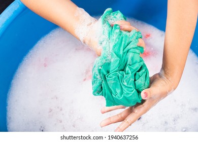 Closeup young Asian woman use hands washing color clothes in basin. Female squeeze wring out wet fabric cloth with detergent have soapy bubble in water, studio shot background, laundry concept