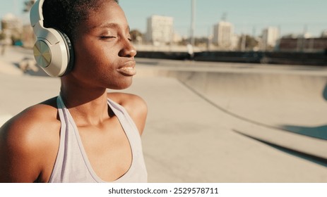 Close-up of young athletic woman sits in a skatepark on a hot summer day, with skateboarders performing tricks in the background - Powered by Shutterstock