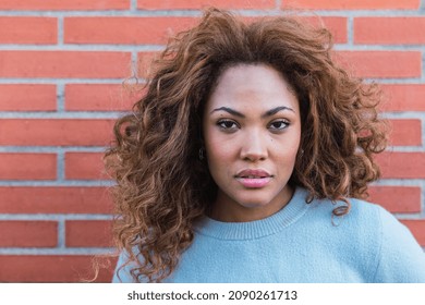 Closeup of young attractive African American model with long afro hair and blue shirt looking at camera while posing in brick wall. Beauty concept - Powered by Shutterstock