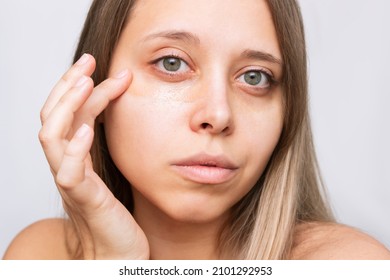 Close-up of a young beautiful caucasian blonde woman applying the tonal foundation for dark eyes. Bruises under the eyes are caused by fatigue, nervousness, lack of sleep, insomnia, stress