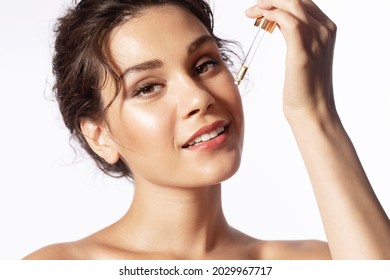 Close-up young beautiful female applying facial serum, using anti-aging treatment product, hydrating and nourishing skin for better tone on white studio background. Natural woman beauty and skincare.