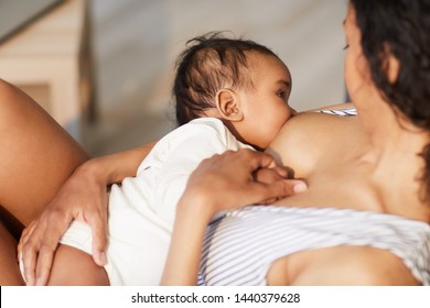 Close-up of young black mother attaching baby at breast while giving nipple to son during breastfeeding