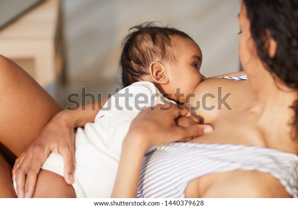 Close-up of young black\
mother attaching baby at breast while giving nipple to son during\
breastfeeding