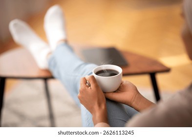 Primer plano de la mujer negra joven que calienta sus manos en la taza de café, relajándose en casa, espacio vacío. Señora irreconocible con la bebida caliente aromática que disfruta del tiempo relajante pacífico en el día libre