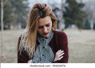 Closeup Of Young Blonde Woman In Park Looking Down With Crossed Arms, Low Confidence 