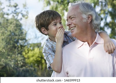 Closeup of a young boy whispering in grandfather's ear outdoors - Powered by Shutterstock