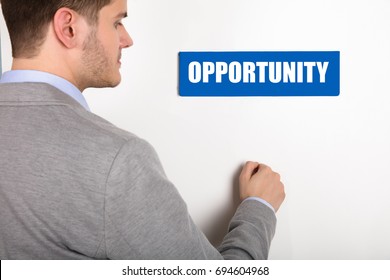 Close-up Of A Young Businessman Knocking White Door With Opportunity Text