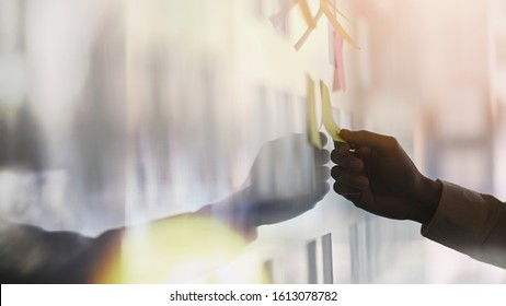 Closeup young businessman while sticky note on glass wall.Sticky note paper reminder schedule board. Brainstorming concept.