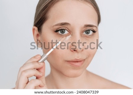 Close-up of a young caucasian attractive blonde woman applying the concealer for dark eyes. Bruises under the eyes. Foundation cream hiding spot imperfections on female face