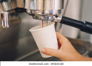 Closeup Of Young Caucasian Barista Hands Holding Paper Cup Making Coffee Using  Coffee Machine. Woman Pouring Coffee From Professional Espresso Machine. Toned With Film Filters.