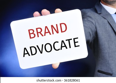 Closeup Of A Young Caucasian Businessman In A Gray Suit Showing A Signboard With The Text Brand Advocate Written In It