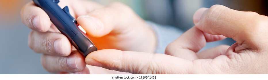 closeup of a young caucasian man about to measure his blood glucose level in a glucose meter by pricking his finger with a fingerstick, in a panoramic format to use as web banner or header