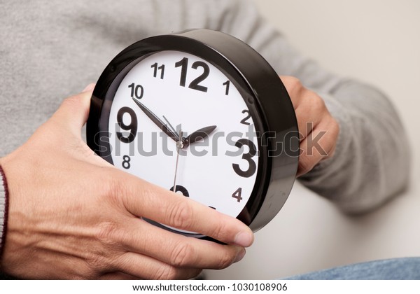 closeup of a young caucasian man adjusting the time\
of a clock