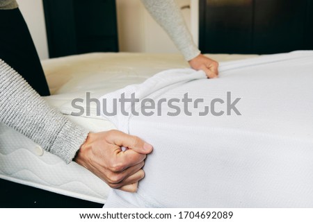closeup of a young caucasian man covering a mattress with a white mattress protector
