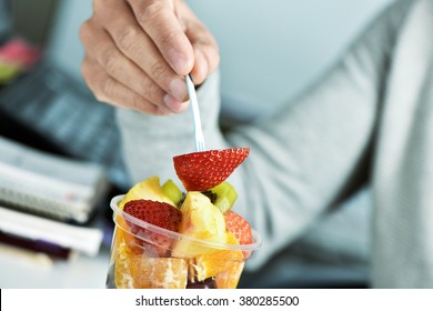 Closeup Of A Young Caucasian Man Eating A Fruit Salad From A Clear Plastic Cup At The Office