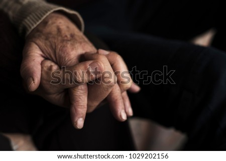 closeup of a young caucasian man holding the hand of an old caucasian woman, with their fingers entwined with affection
