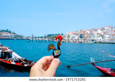 closeup of a young caucasian man holding a traditional Rooster of Barcelos, the emblem of Portugal, in Porto, at the Douro River with the Ribeira district on the right