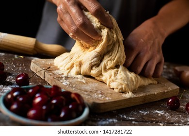 closeup of a young caucasian man kneading a piece of dough to prepare a coca de cireres, a cherry sweet flat cake typical of Catalonia, Spain, on a wooden table
