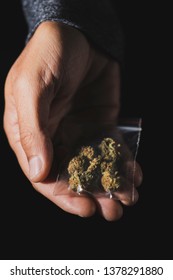 closeup of a young caucasian man with a plastic bag with some marihuana buds in his hand, against a black background